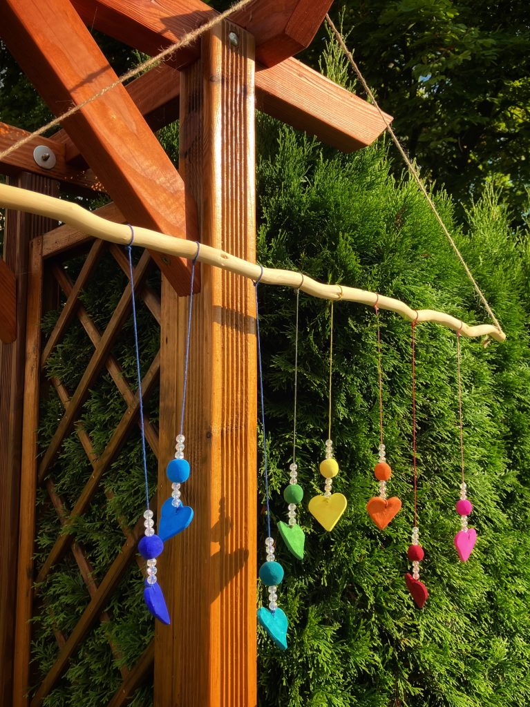 Ein gebasteltes Windspiel mit bunten Herzen, das im Garten hängt.